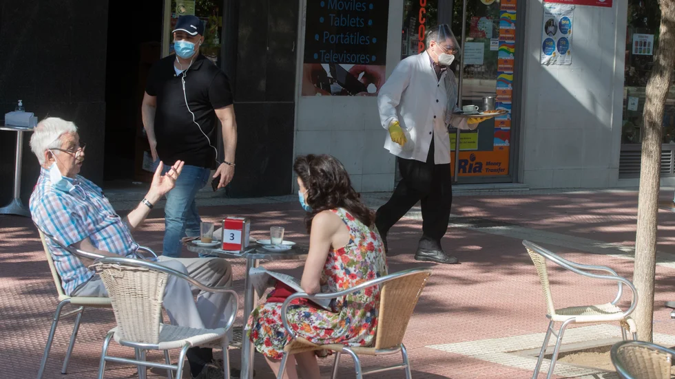 En kypare i munskydd och handskar serverar gästerna i Madrid på måndagen, när uteserveringar i huvudstaden och i Barcelona tilläts öppna igen.