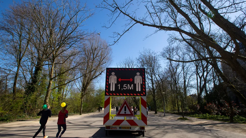 Två joggare i Amsterdam framför en skylt där de uppmanas att hålla avstånd. Nu införs en regel om att polisen får lov att upplösa grupper på mer än tre personer.