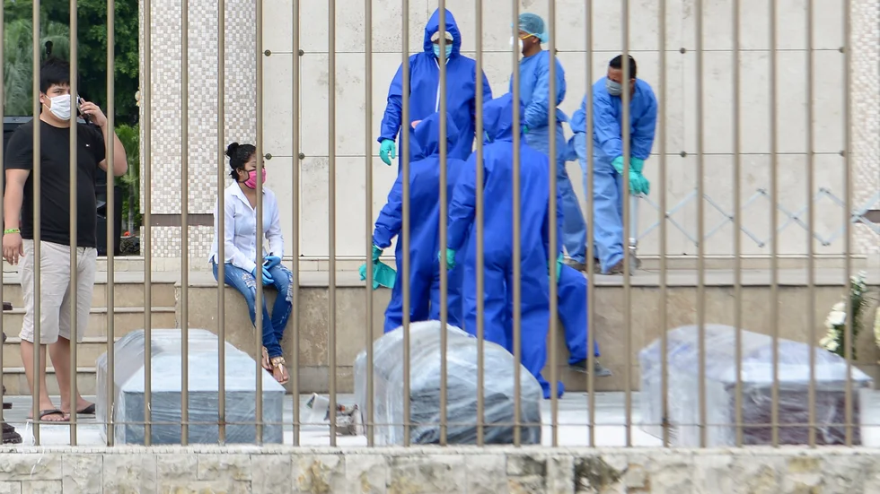Plastinlindade kistor bärs iväg av människor i skyddsmundering i Guayaquil.