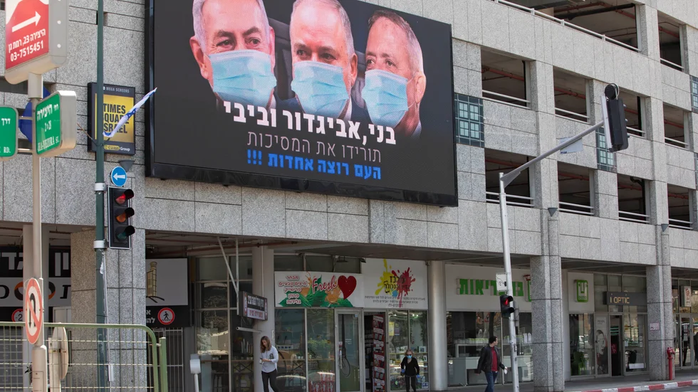 Israels premiärminister Benjamin Netanyahu isolerar sig efter att möjligen ha kommit i kontakt med en smittad medarbetare vid ett knesset-sammanträde. Skylten på bilden sitter i Tel Aviv och visar Netanyahu och ledarna för de två främsta oppositionspartierna, Benny Gantz och Avigdor Lieberman.