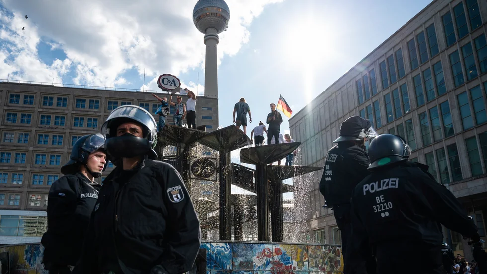 En brokig skara demonstranter protesterar mot coronarestriktioner uppe i en fontän på Alexanderplatz i Berlin.