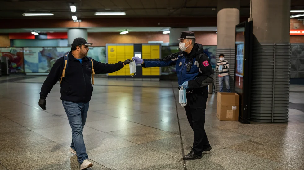 En morgonpendlare tar emot ett andningsskydd av en polisman vid tågstationen Atocha i Madrid under måndagsmorgongen.