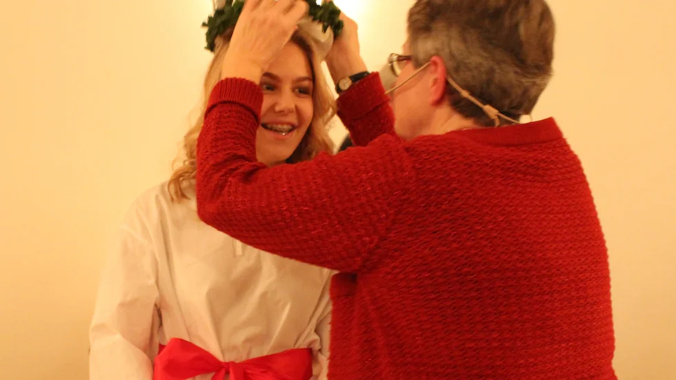Missionsförsamlingens ordförande Ann.Christin Ohlsson får med visst besvär men med gott humör Luciakronan på plats på Emma Olovssons huvud.