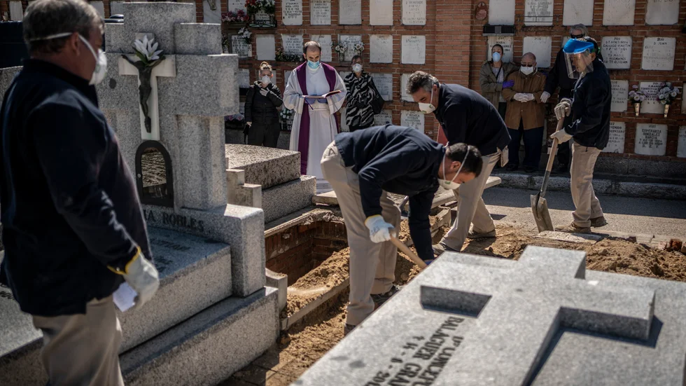 En präst och anhöriga ber en bön i samband med att en person som avlidit i covid-19 begravs på en kyrkogård i Madrid.