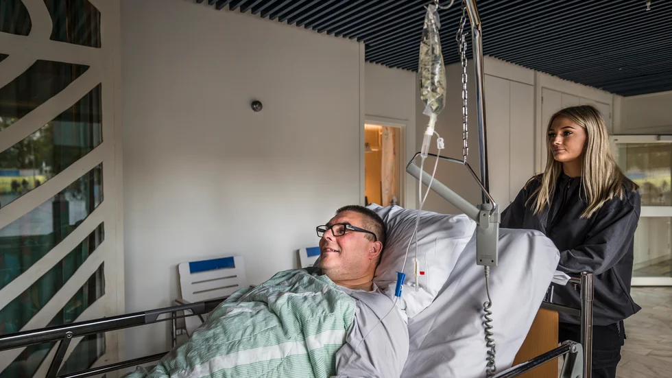 Tenho Kilpijärvi har väntat nästan ett dygn på vårdplats. Under natten hade han ett eget rum på akuten, men på morgonen skjutsades han ut till korridoren, vilket han tyckte var helt okej. Här skjutsas han till ortopedavdelningen av transportören Klara Holm. 