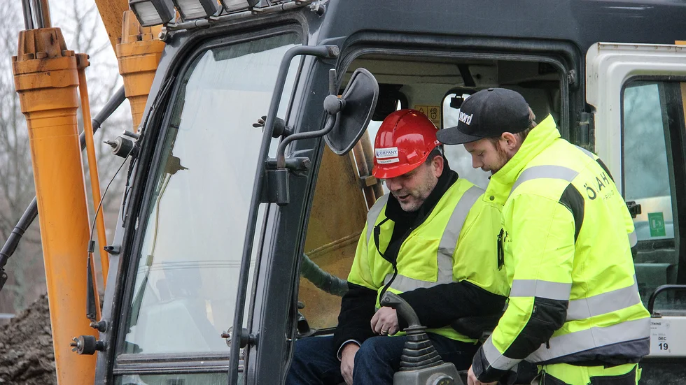 Kommunalrådet Ingvar Smedlund i röd hjälm får en kort instruktion av grävmaskinisten Martin Öjdahl inför första grävtaget för radhusen i Gamla Nynäs.