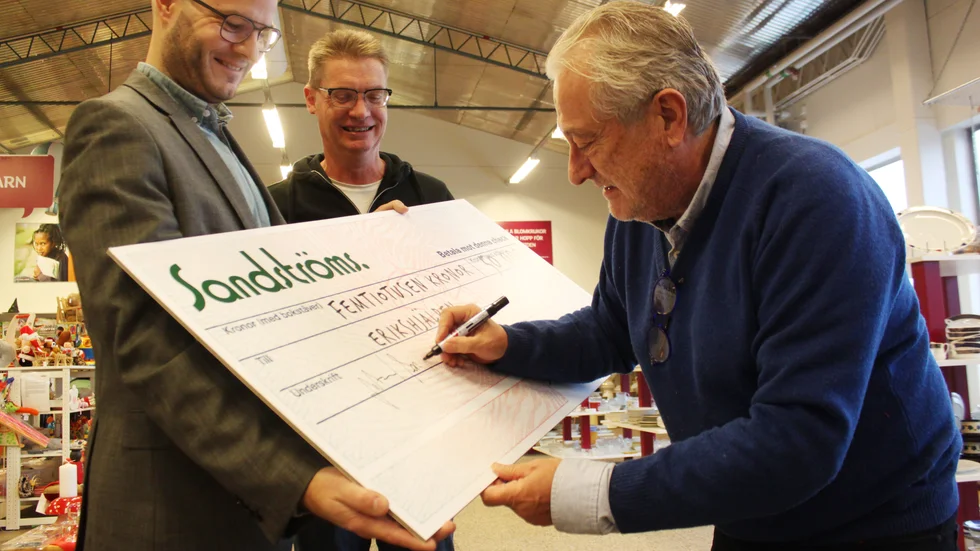 Mikael Sandströms undertecknar en symbolisk check på 50 000 kronor. Daniel Måledal och Peter Magnusson, Erikshjälpen, tar emot.