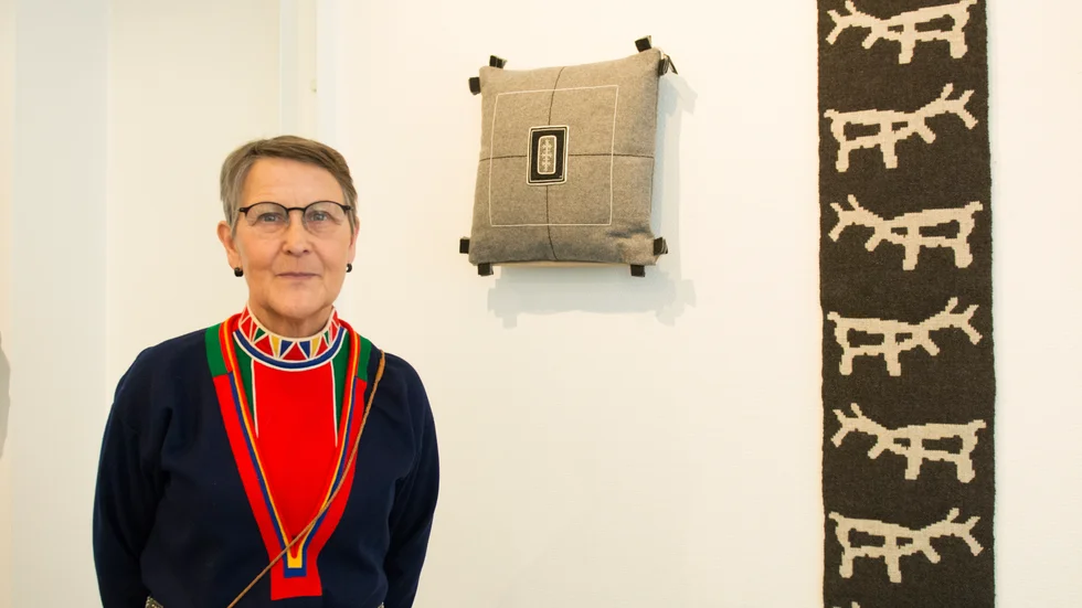 Gunhild Tjikkoms utställning öppnade på torsdagen. Bakom henne syns kudden Dálvvevinndek/Vinterfönster" och väven "Elva renar".