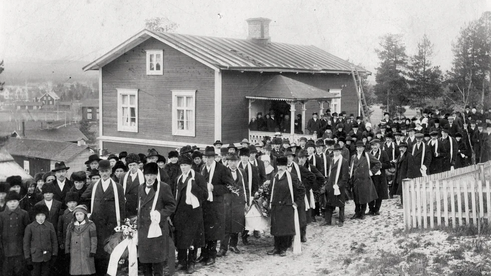Älvsbyn i oktober 1918. Samling på Hanna Lundströms café (nuvarande Selholmsvägen 4) före begravningen av bland andra Nils och hans fosterbarn. Alla som skulle begravas hade dött av spanska sjukan. Public Domain.