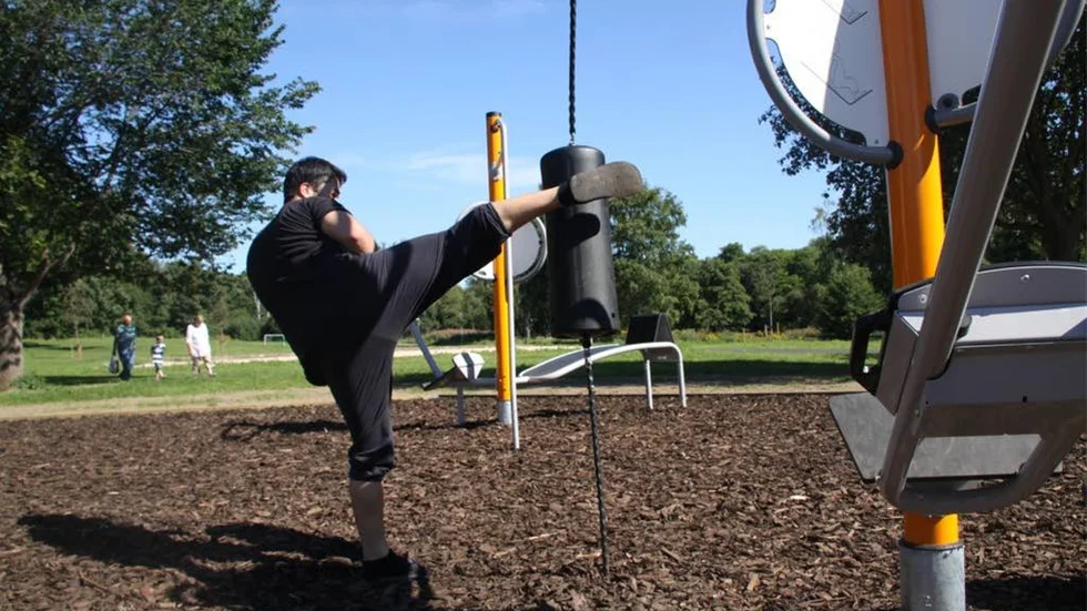 Usman Numanov glädjs åt det nya friluftsgymmet på Prästgårdsängen, och efter fotografens önskemål provade han även slagpåsen.