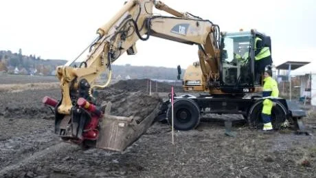 Fjärrvärmen transporteras i en 11 kilometer lång överföringsledning mellan orterna. Ledningen läggs på 60 centimeters djup. Här får Magnus Berge hjälp med det första skoptaget av Henrik Johansson Casimiro och maskinisten Henrik Jonsson. Foto: Titti Olovsson