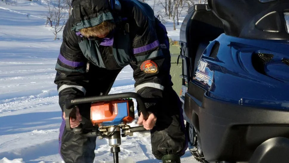 Valborg borrar alltid första hålet nära snöskotern. Då kan hon sitta på den och fiska när hon behöver vila.