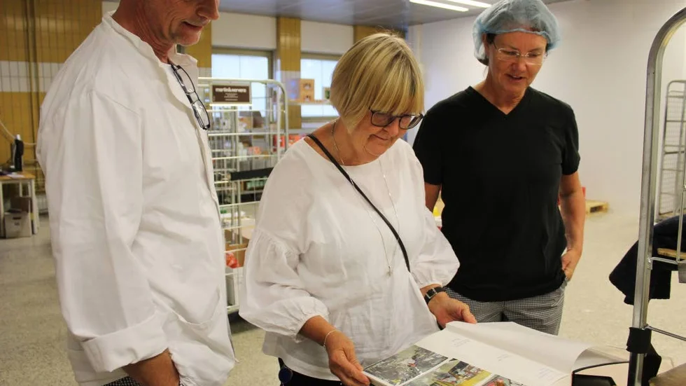 Ulf Johansson, Karin Ekström och Marie Lindqvist bläddrar i ett album med gamla bilder från deras arbetsplats.