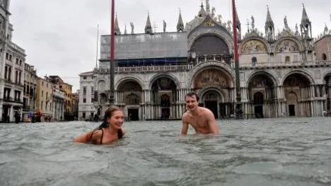 A young man and a woman enjoy swimming in flooded St. Mark's Square in Venice, Italy, Sunday, Nov. 11, 2012. High tides have flooded Venice, leading Venetians and tourists to don high boots and use wooden walkways to cross St. Mark's Square and other areas under water. Flooding is common this time of year and Sunday's level that reached a peak of 58.66 inches (149 centimeters) was below the 63 inches (160 centimeters) recorded four years ago in the worst flooding in decades. (AP Photo/Luigi Costantini)
