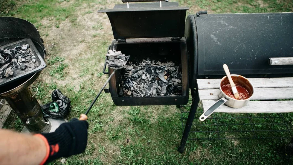 I den vanliga grillen till vänster förbereds kolen, som sedan läggs  i behållaren som hänger vid sidan av smokern.