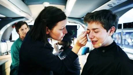 Sminkas. Innan studioinspelningen i bussen blir barnreportern Anthon Bremer sminkad. Sedan ska han in på SSAB för att lösa en uppgift genom att intervjua järnverksarbetare.