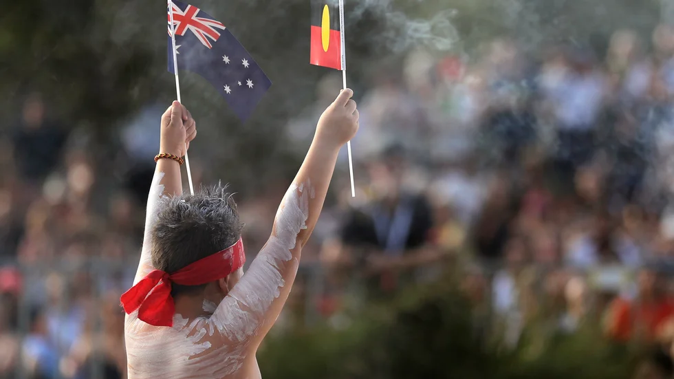 Den australiska och den aboriginska flaggan hålls upp av en man från ursprungsfolksgruppen under fjolårets firande av den australiska nationaldagen.