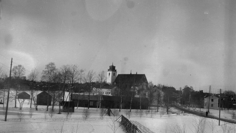 Utsikt mot Gammelstads kyrka från Hedqvists hus, Lulevägen 12, omkring 1940. Vägen syns till höger. Det stora ljusa huset nedanför kyrkan är nuvarande Margaretas värdshus. Vid det bortre snöstaketet invigdes 1944 Nederluleå kommuns nya kommunalhus. I tvåvåningshuset längst till höger fanns Bergströms Ur & Pappershandel och på övervåningen telefonstationen som startade 1898.