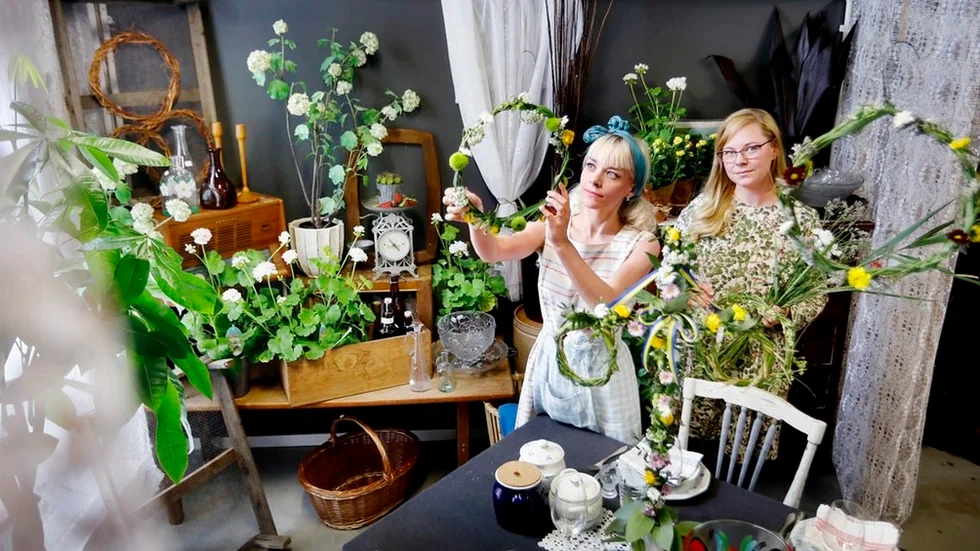 Många gröna växter, midsommarstång på bordet och blomsterkransar i taket. Maria och Karin Larsson, som har butiker i Retuna, tipsar om hur man får midsommarkänsla även om lunchen eller kvällens middag blir inomhus.