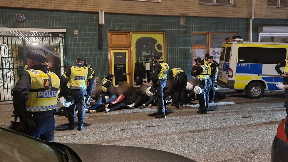 Personerna som omhändertagits sitter uppradade på trottoaren på S:t Persgatan. 
