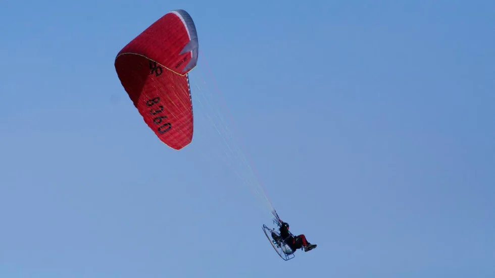Paramotor. Flygaren hänger under en så kallad friflygskärm och har motor med propeller på ryggen.