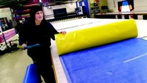 Karin Brüggemann arbetar med de ljuddämpande draperierna som är en viktig del av Gigant Miljötekniks produktion. Hon har precis svetsat fast ett ljudabsorberande material på ena sidan av gummiduken och utanpå ett nät som släpper in ljudet. Draperier av det här slaget används främst vid arbete med högfrekventa maskiner.