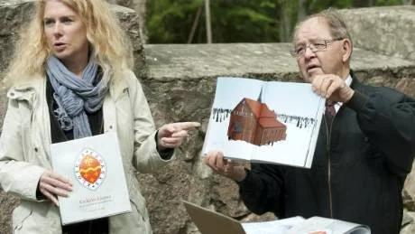Ulf Svensson håller upp en illustration av klosterkyrkan i Krokek, som finns med i den nya bok, som Marie Ohlsén, på bilden, skrivit.  - Jag hoppas att vi även kan bygga en modell av kyrkan och ställa upp här vid Krokeks ödekyrka, sa Ulf Svensson. Foto: Robert Svensson
