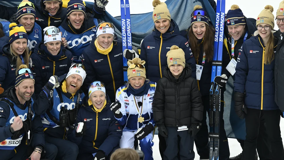 Kronprinsessan Victoria, prins Daniel, prinsessan Estelle och prins Oscar poserar för en gruppbild med det svenska längdlandslaget – bland andra Frida Karlsson, Jonna Sundling och landslagschef Anders Byström – efter söndagens avslutande femmil på skid-VM i Trondheim.