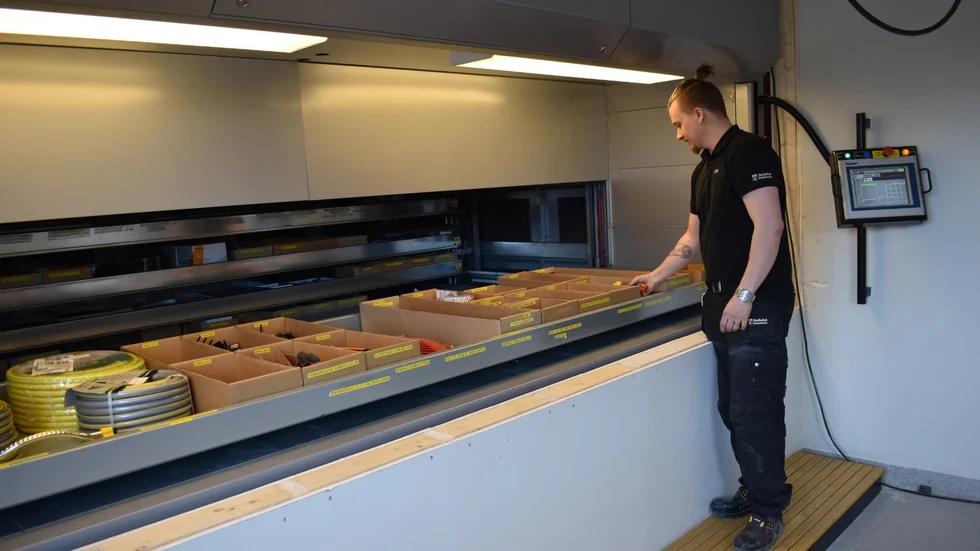Johan Zakrisson lägger de sista prylarna i lagerautomaten. Detta är hylla 18, och där finns trädgårdsgrejer av olika slag. Automaten styrs med reglaget strax bakom honom. 