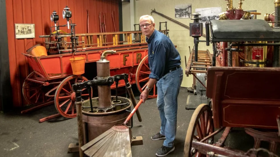 Gunnar Wagenius vid Brandkårsmuseet i Simonstorp visar en plåtkvast, som ju var bättre än en granruska. I bakgrunden en hästdriven brandvagn från 1865.