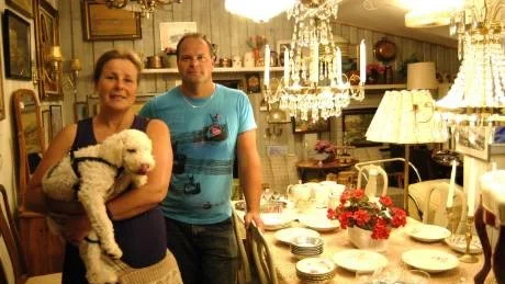 Christina Larsson-Bhiladvala med hunden Zita i famnen har övertagit Isacssons antikhandel i Gamleby som Kenth Isacsson, i bakgrunden drivit i Gamleby i 20 år.
