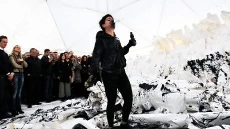 Inferno. Det vita, sakrala har förvandlats till ett bläckfläckat inferno i Moderna museets tältpalats Bucky dome. Konstnären Anastasia Ax tvekar inte att förstöra sina skulpturala verk under performanceföreställningen.