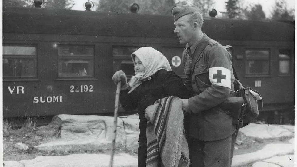 Svensk militär sjukvårdare hjälper finsk äldre kvinna som anlänt med flyktingtåget till Haparanda hösten 1944.