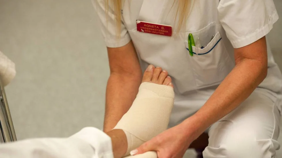 En undersköterska lindar foten på en patient.