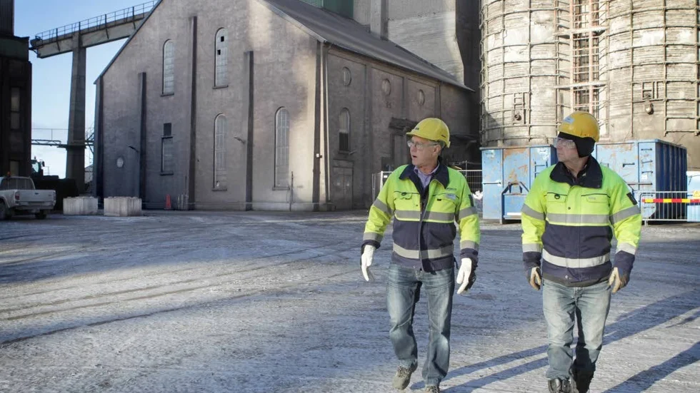 Bo Persson och Henning Andersson började båda jobba vid Cementa på 1960-talet. Nu är båda pensionärer, men sköter varje sommar guidningarna på fabriksområdet. I bakgrunden (t.v) syns en del av fabrikslokalerna som stod färdiga 1919.