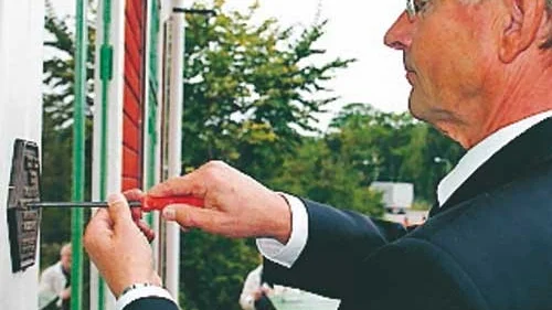 Landshövding Sven Lindgren i full färd med att skruva fast skylten som talar om att Virserums station har blivit byggnadsminnesmärkt.