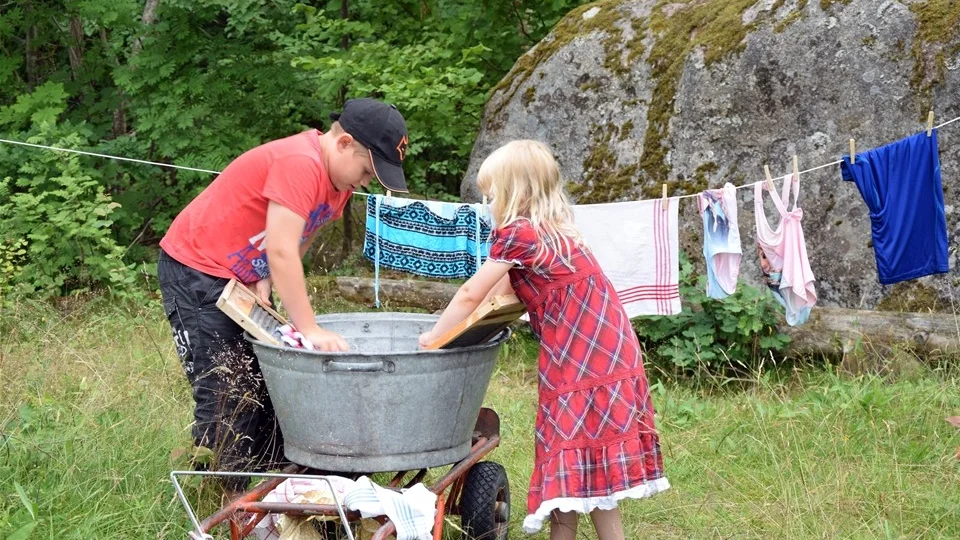 Syskonen Helmer och Vera Landberg testar att tvätta med hjälp av balja och tvättbräda.