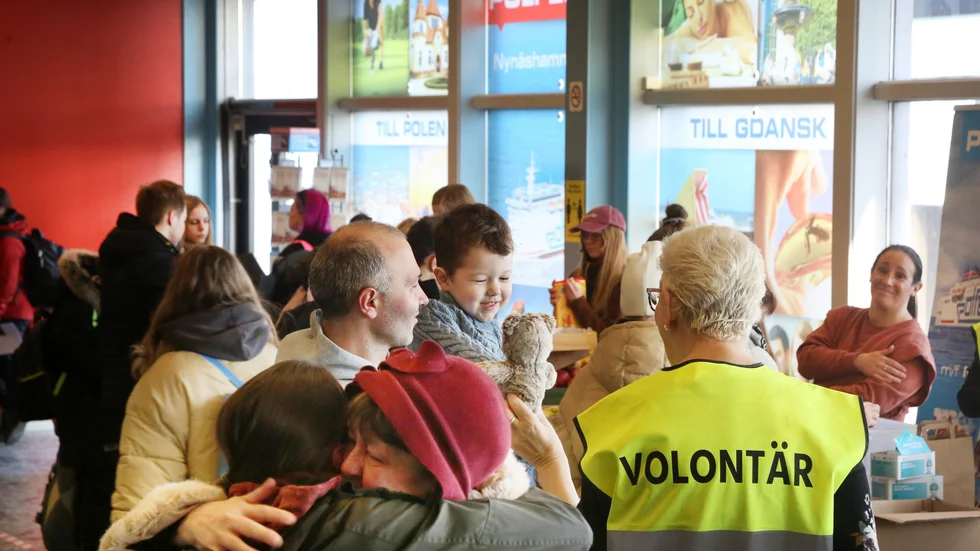 Flyktingpojken David, 3 år, i sin pappas famn får en nalle av volontären Birgitta Welander vid ankomsten till Nynäshamn.