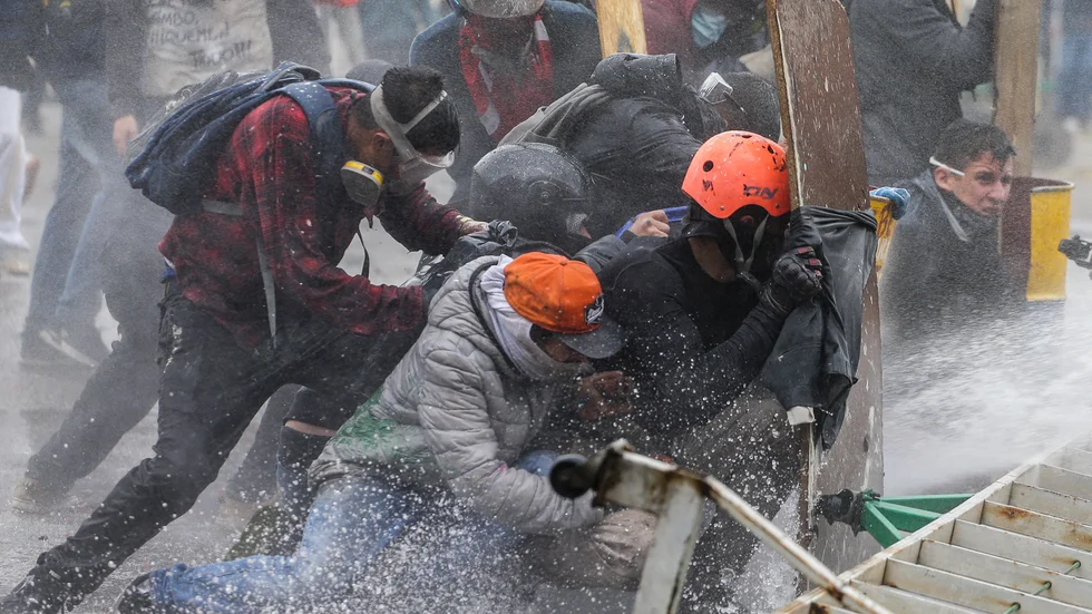 Demonstranter tar skydd för polisens vattenkanoner utanför Colombias huvudstad Bogotá under fredagen.