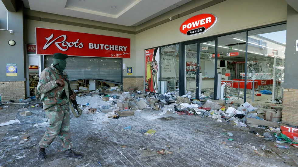 En soldat patrullerar vid ett plundrat köpcentrum i Soweto utanför Johannesburg.