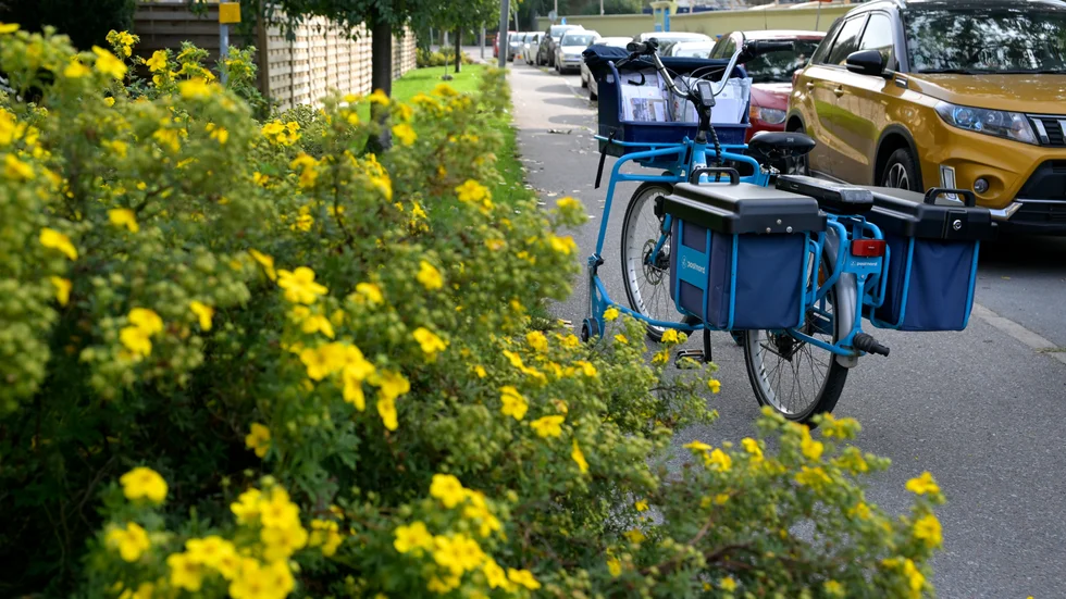 En parkerad blå postcykel från Postnord i ett radhusområde.
