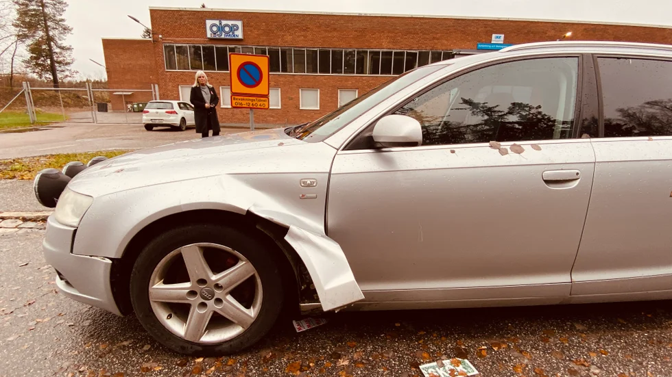 En övergiven bil med punktering och trasig framskärm står parkerad precis utanför Ojop. Intill den ligger en trasig övningskörningsskylt.