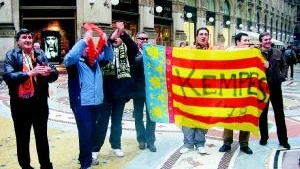 Beskedliga. En liten grupp beskedliga supportrar från spanska ligalaget Valencia sjunger och dansar inför ett tv-team inne i den grymt stora gallerian vid Piazza del duomo i Milano. Ute på piazzan vakar gravallvarliga halvmilitära poliser för att förhindra varje tendens till huliganism.FOTO: HANS BRANDIN