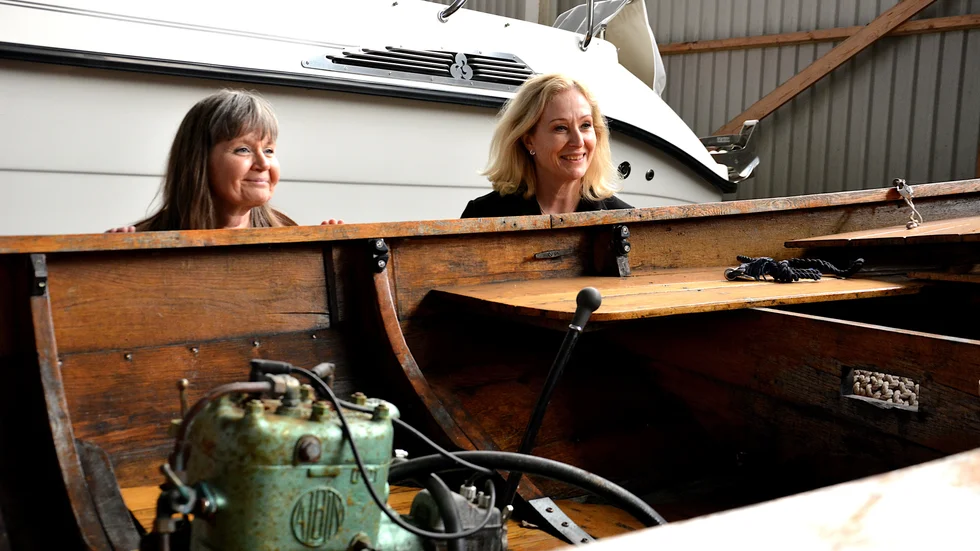Regionrådet Eva Andersson (S) och kulturminister Jeanette Gustafsdotter tittar ner i en klinkbyggd båt i verkstaden hos Waldemarsviks träbåtsförening.