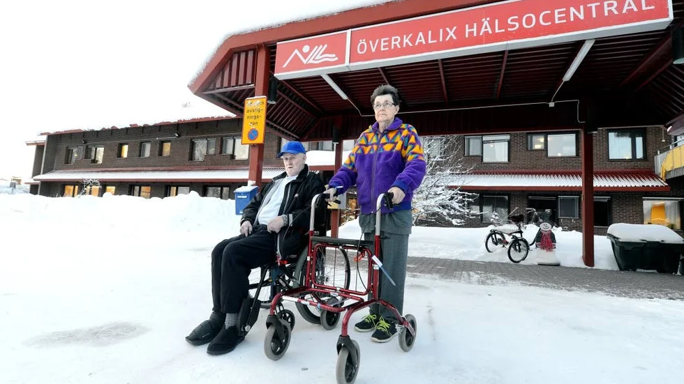 UTE I KYLAN. När det inte fanns någon plats på hemsjukhuset i Kalix lades 73-åriga Cathrine Lindborg in på obs-avdelningen på hälsocentralen i Överkalix – vilket har betytt 14 mils resväg med färdtjänst tur och retur för hennes jämngamla make Börje Lindborg i rullstol. Fotoförbud inomhus hindrade inte paret från att ställa upp på bild.
