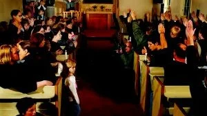 De homosexuellas situation i Sverige idag, konstnärligt gestaltad av Elisabeth Ohlson Wallin  och med kyrkans mittgång som vattendelare mellan två skilda världar. Vad ser vi? Ett kyrkorum, anonymiserat; kunde vara var som helst. Men, märker man genast, så mycket som inte stämmer. En sådan utsatthet bland människorna till vänster, man kommer att tänka på fartyg i nöd. Människor som värjer sig, klamrar sig fast vid varandra. Den lilla flickan, som håller mamma i handen. Spädbarnet som ingenting förstår. Det unga paret, som hos varandra glömmer omvärlden. Och så den andra sidan; med alla dessa händer hotfullt lyfta  kanske till den hälsning, som vi alltför väl känner till. Med mannen, som blåser ut det sista tända ljuset på denna onda sida. Och därborta predikanten, med djävulsskugggan på väggen bakom sig... Hon vill, säger hon, göra bilder som får folk att tänka. Att uppfatta människorna till vänster som utsatta, nödställda är helt rätt.  Och så utsatta känner vi homosexuella oss idag, förklarar hon.