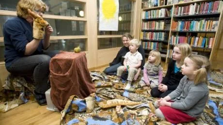 - Här är älgen som är arg på gärdsmygen som sitter på hans näsa...berättar bibliotekarie Inger Linnarsson för barnen som sitter andäktigt och lyssnar på dockteatersagan i Östra Husbys bibliotek. Från höger Stella och Smilla Runqvist, Wilma Hansson och Jonas Åsenklint i barnskötaren Harriet Anderssons knä.Foto: Robert Svensson