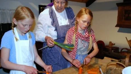 Vånga hembygdsförenings Eivor Sandberg instruerar Emilia Kindahl och Rebecka Ridderborger hur man gör grönsakssoppa. Här skivar de morötter.