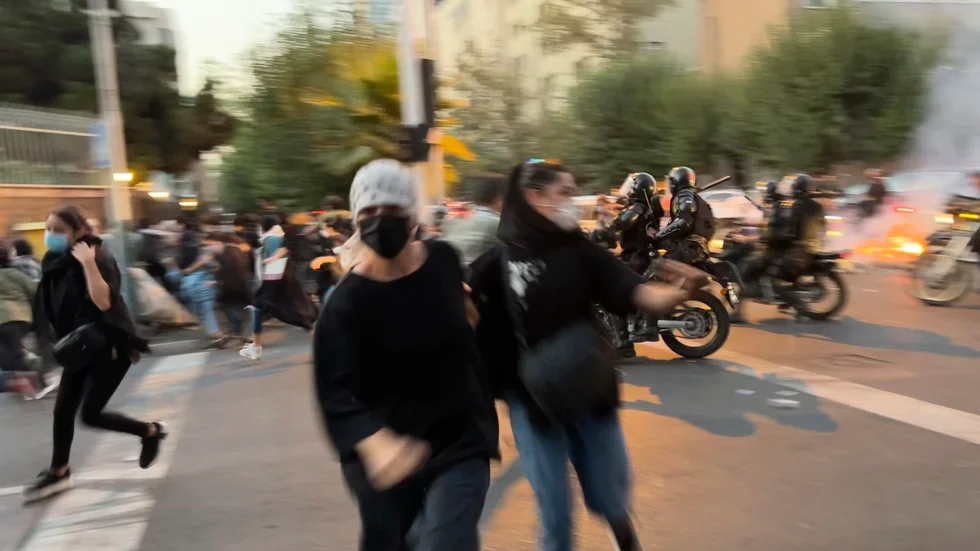 Två kvinnor och flera andra personer flyr när iransk kravallpolis kör emot dem på motorcyklar, vid en av de tidiga protesterna i Iran i september förra året. Arkivbild.