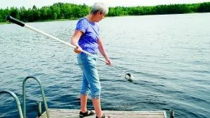Miljö- och hälsoinspektören i Finspångs kommun, Kerstin Andersson kontrollerar att vattenkvaliteten är god. Här vid badet vid SMU Bönergården. I den lilla behållaren samlas ett vattenprov som skickas för analys. Svar kommer om en vecka. Foto: Ellinor Lundmark
